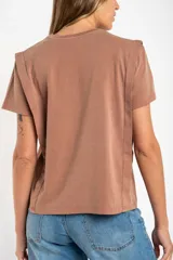 Remera de algodón color mostaza/naranja quemado, con cuello redondo y mangas cortas. Presenta un diseño con costuras externas visibles en los hombros y laterales, dándole un aspecto desestructurado.