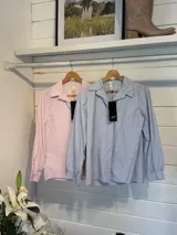 Camisa de manga larga con diseño de rayas verticales en tonos celeste y blanco. Presenta cuello clásico, cierre frontal con botones y mangas con puños acampanados con volados.