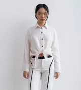 Camisa negra de manga larga, con cuello camisero y botones frontales. Presenta aberturas laterales en el ruedo.