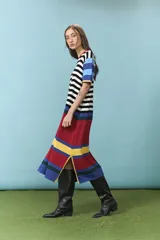 Vestido midi de algodón con diseño de rayas horizontales en color blanco y negro en el torso, mangas cortas con bloques de colores celeste, azul, verde y amarillo, y parte inferior con franjas anchas en rojo, amarillo y azul. Cuenta con cuello redondo ribeteado en rojo.