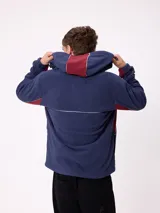 Campera de polar con cierre frontal, capucha ajustable y diseño con bloques de color azul marino y detalles en bordó. Presenta el logo de la marca bordado en el pecho.