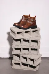 Bota corta color marrón óxido, con suela track negra, doble correa con hebillas plateadas y detalle de ojales.