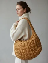 Bolso tipo hobo capitoneado color mostaza, con diseño acolchado y correa integrada al cuerpo del bolso. Cuenta con cierre superior y forro interno.