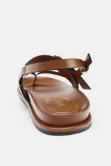 Sandalia plana color marrón con tiras de cuero y hebillas metálicas doradas.