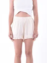 Short de tela liviana color crema, con cintura elástica y cordón de ajuste. Presenta un diseño holgado con detalle de volados en el ruedo.