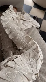 Pantalón de lino color beige con diseño de tablas verticales aplicadas que aportan textura y movimiento. Presenta tajos laterales, bolsillos delanteros y traseros, y un corte holgado.