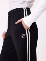 Pantalon de jogging de corte ancho, color negro con rayas laterales blancas. Posee cintura elastizada con cordón de ajuste y logo bordado en la parte frontal.