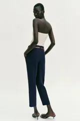 Pantalón tobillero de tiro medio, color azul marino, con bolsillos delanteros y cierre frontal con cremallera, botón y gancho. Incluye un cinturón fino de color marrón con hebilla metálica.