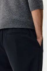Pantalón sastrero de corte slim fit y color negro, con cierre frontal de botón, bolsillos laterales al bies y bolsillos posteriores ojalados. Cuenta con trabillas para cinturón y pretina elástica en la parte posterior.