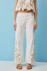 Pantalón negro de tiro alto y corte recto, confeccionado con detalles de bordados florales calados en la parte inferior de las piernas.