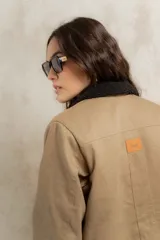Campera color beige con cuello de corderito negro, cierre frontal con botones y forro interior. Presenta un diseño de corte recto y mangas largas con puños vueltos.