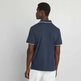 Remera polo azul marino de piqué de algodón, con cuello clásico con ribete blanco, tapeta de dos botones y mangas cortas con ribete blanco.