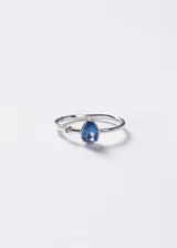 Anillo de plata 925 con diseño minimalista, presenta un cristal azul en forma de gota y un pequeño punto de luz lateral.