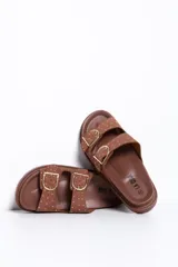 Sandalias de dos tiras en color camel con hebillas metálicas doradas y tachas decorativas, de suela plana y anatómica.
