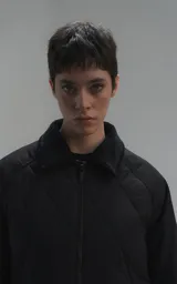 Campera oversize de microfibra opaca con diseño matelaseado de rombos. Presenta cuello de corderoy a tono, cierre frontal metálico y dos amplios bolsillos delanteros con solapa y broche snap. Interior forrado y relleno con guata térmica.