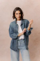 Camisa de denim de lavado medio con calce oversize, cuello camisero, cierre frontal con botones y bolsillos aplicados en el frente.