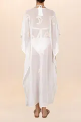 Kaftán largo de algodón traslúcido en color blanco marfil, con diseño amplio, mangas murciélago y bordados sutiles en tono beige. Presenta escote en V con cordones ajustables terminados en borlas.