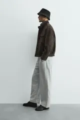 Cazadora de corte relajado confeccionada en piel con acabado de ante. Presenta cuello subido, cierre frontal de cremallera oculta por solapa con botones a presión, bolsillos de plastrón con solapa en el pecho y bolsillos de vivo en la cadera. Incluye trabillas en los hombros, mangas largas con puños abotonados y bajo con elástico.