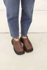 Suecos marrones de cuero con costuras decorativas y suela track negra.