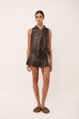 Top sin mangas de cuero color marrón oscuro, con cuello tipo camisa y cierre frontal anudado con tiras de cuero. Presenta pespuntes contrastantes en color claro.