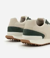 Championes de estilo jogging con diseño de paneles en tonos beige y verde oscuro. Presentan una combinación de malla técnica y refuerzos en material sintético, con suela dentada en color marrón y entresuela blanca.
