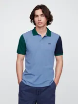 Remera polo de manga corta con diseño color block, cuerpo en azul claro, cuello en verde y mangas en verde y azul marino. Presenta cierre frontal con botones y logo de la marca bordado en el pecho.