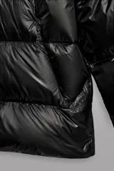 Campera puffer negra con capucha ajustable, cierre frontal con cremallera, bolsillos laterales con cremallera oculta y relleno de plumón y pluma.