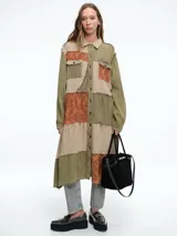 Vestido camisero largo de estilo patchwork con cierre frontal de botones, cuello clásico y mangas largas. Presenta una combinación de texturas y estampados en tonos tierra, verde oliva y naranja con bordes deshilachados.