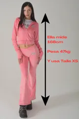 Conjunto de dos piezas confeccionado en terciopelo rosa, compuesto por un buzo con capucha y cierre frontal, y un pantalón de corte acampanado. Ambas prendas presentan un estampado gráfico circular con el número 27.