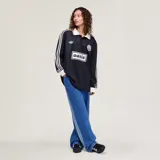 Camiseta Adidas de manga larga en colaboración con la banda Oasis, de color negro con cuello polo, puños y detalles en blanco marfil. Presenta las tres tiras características en las mangas, el logo trébol de Adidas, un escudo circular conmemorativo de la gira 'Live '25' y el estampado con la inscripción 'oasis' en el centro del pecho.