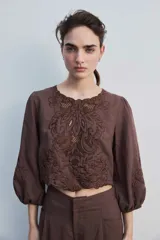 Blusa negra con detalles de apliques bordados en el pecho y las mangas, cuello redondo y mangas largas abullonadas.
