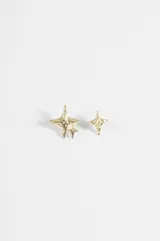 Par de aros asimétricos dorados con diseño de estrella de cuatro puntas, acabado texturizado y un pequeño detalle de piedra clara en el centro de uno de ellos.