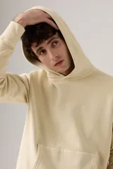 Buzo hoodie color crema con logo bordado en el pecho y bolsillo tipo canguro.