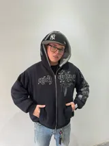 Campera reversible con cierre frontal, diseño oversize. Un lado es de algodón negro con estampados y bordados gráficos, mientras que el otro lado es de tela polar gris de pelo largo. Cuenta con capucha, puños y ruedo acanalados.