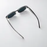 Lentes de sol con armazón ovalado de policarbonato gris traslúcido y cristales oscuros, con filtro UV400 y diseño versátil.