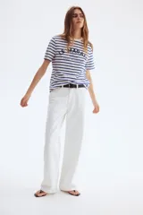 Remera de manga corta con cuello redondo, confeccionada en tejido de punto a rayas horizontales blancas y azules. Presenta un estampado frontal con texto en negro que incluye "LE MARAIS" y "Paris".