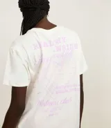 Remera blanca de algodón de corte oversized, con cuello redondo y mangas cortas. Presenta estampa en la espalda con texto y diseño gráfico en color lila.