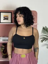 Top corto de algodón negro con breteles finos y ajuste al cuerpo. Presenta un pequeño aplique decorativo circular en el centro del pecho.