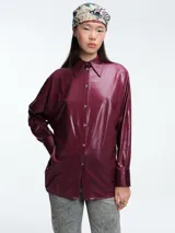 Camisa de corte oversize confeccionada en tejido brillante con acabado satinado. Presenta cuello en punta, cierre frontal con botones, mangas largas con puños anchos y tajos laterales en el ruedo.