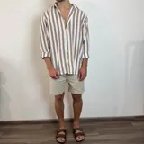 Camisa de lino de corte oversize con diseño de rayas verticales en tonos blanco y tostado, manga larga y cierre frontal con botones.