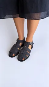 Sandalias cangrejeras de gamuza color marrón, con punta redonda, taco bajo, talonera cerrada y tira con hebilla metálica ajustable en el tobillo.