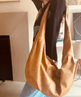 Bolso tipo hobo de cuero color camel, con correa ancha para el hombro y bolsillo interno con cierre.
