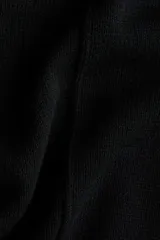 Top de punto negro con costura central delantera, mangas cortas con hombros caídos y ribete acanalado en cuello, puños y bajo.