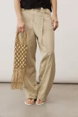 Cartera de mano de macramé color crudo con apliques de caracoles y flecos colgantes en la parte inferior. Cuenta con asas rígidas integradas en el mismo tejido.