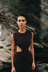 Vestido midi de color negro, sin mangas, con cuello redondo y aberturas laterales en la cintura (cut out). La parte superior es de punto liso y la falda presenta una textura plisada y ligera.
