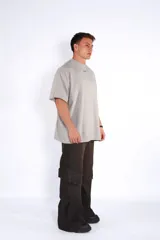 Remera oversize de algodón color gris claro, con cuello redondo y manga corta. Presenta un pequeño logo bordado en azul en el pecho.