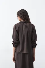 Camisa negra de corte relajado y caída fluida, con cuello clásico, escote en V y cierre frontal con botones forrados. Presenta mangas largas con puños abotonados.