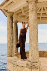 Vestido largo color chocolate con tirantes finos, escote recto y detalle de nudo en la cintura que crea una abertura en la falda.