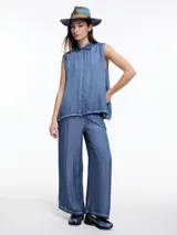 Camisa sin mangas color beige claro con efecto teñido en frío y aspecto gastado. Presenta cuello clásico, cartera oculta y ruedo irregular, más largo en los laterales.