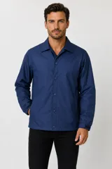 Campera estilo coach de poliéster color azul, con cuello camisero, cierre frontal con botones a presión y bolsillos laterales.